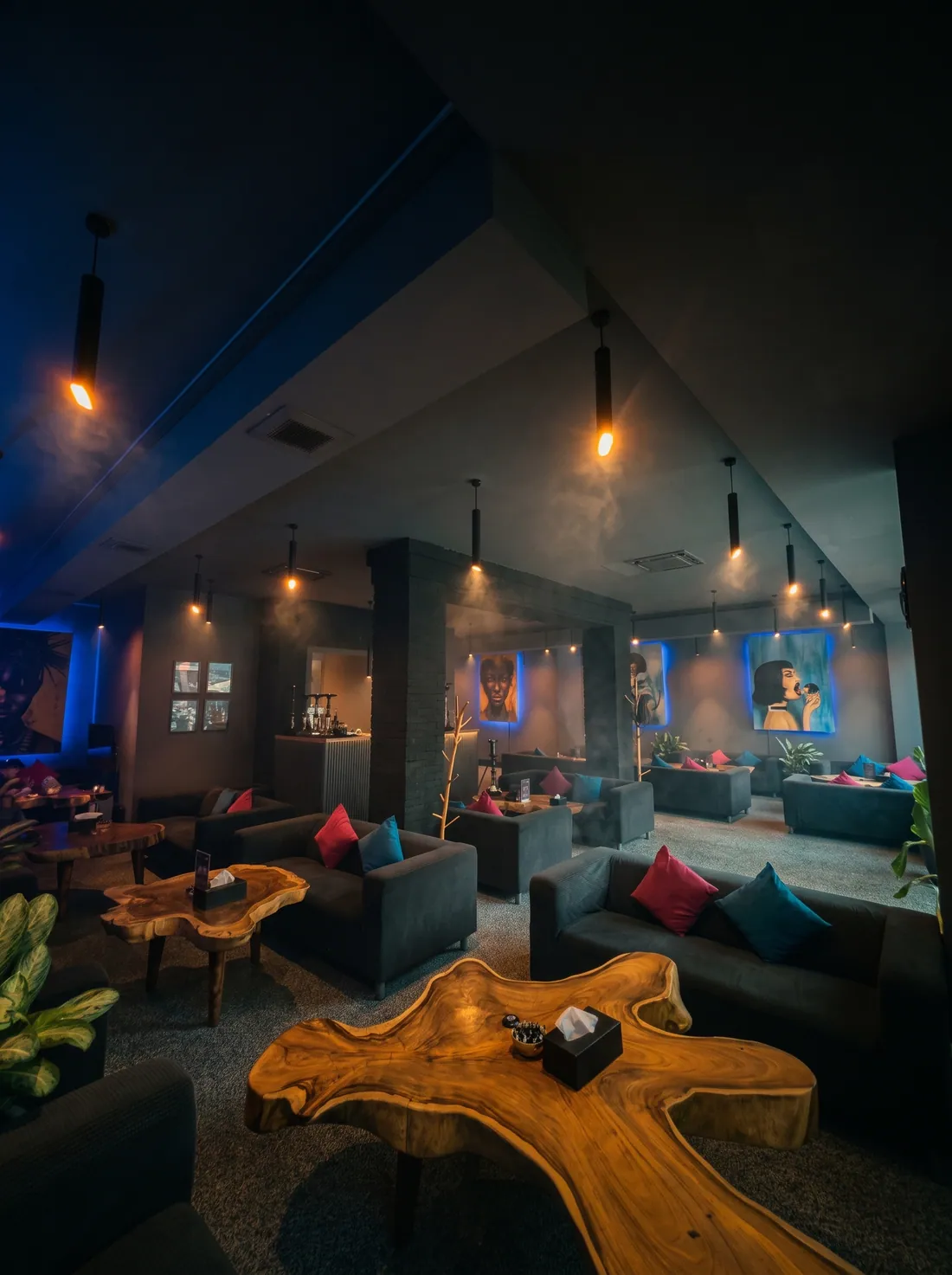 Main hall with grey sofas, live-edge wooden tables, warm pendant lamps and backlit paintings